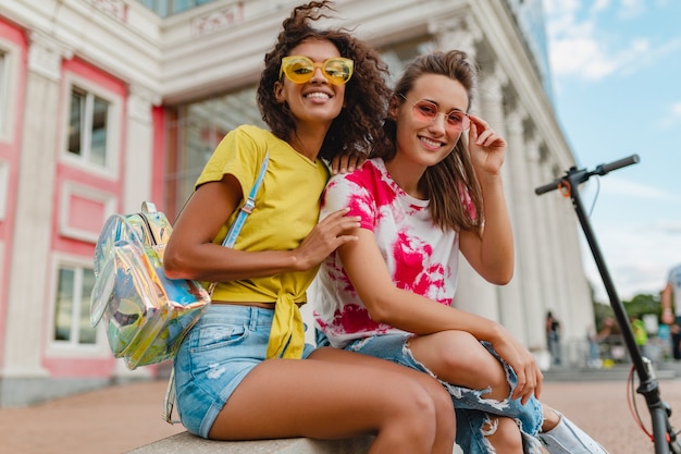 Amigos de meninas felizes e elegantes sorrindo sentados na rua, mulheres se divertindo juntas