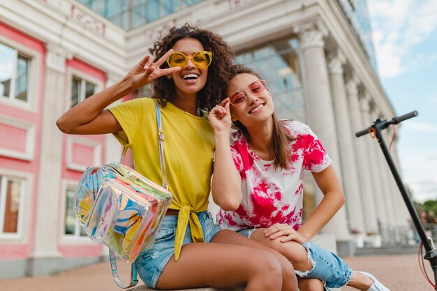 Amigos de meninas felizes e elegantes sorrindo sentados na rua, mulheres se divertindo juntas