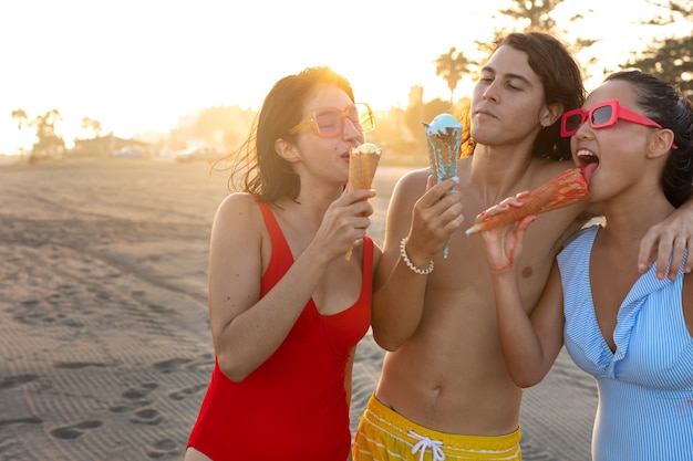 Amigos de tiro médio tomando sorvete na praia