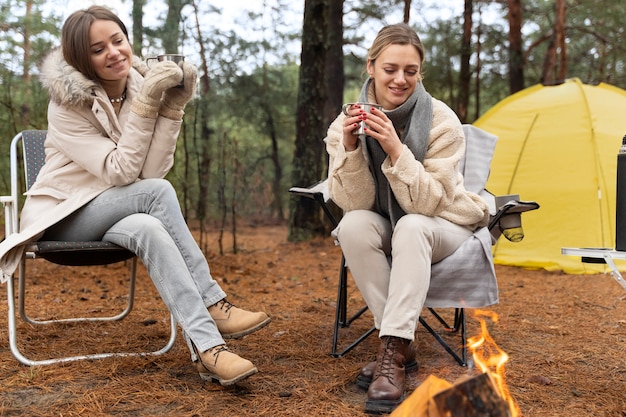 Amigos do sexo feminino bebendo água por uma fogueira durante o acampamento
