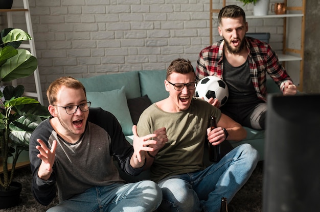 Foto grátis amigos do sexo masculino alegres assistindo esportes na tv com futebol