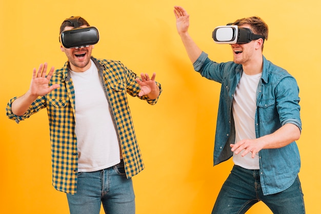 Foto grátis amigos do sexo masculino jovens felizes usando óculos de realidade virtual, tirando sarro, contra um fundo amarelo