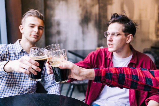 Amigos do sexo masculino tilintar os copos de cerveja por cima da mesa