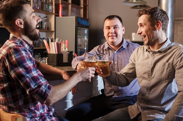 Amigos felizes bebendo cerveja no balcão no pub