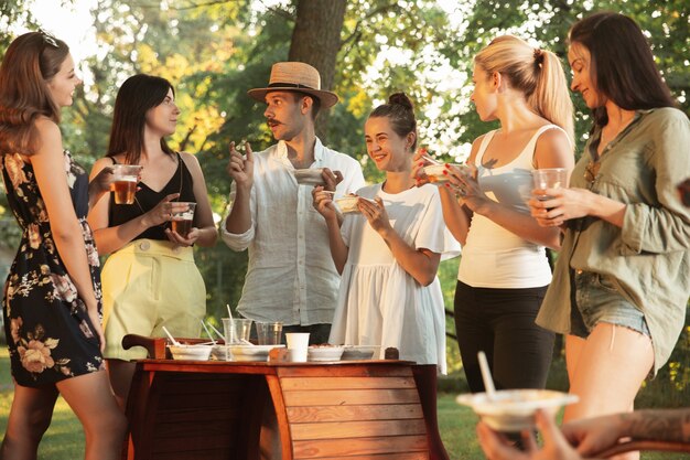 Foto grátis amigos felizes comendo e bebendo cerveja em um jantar de churrasco na hora do pôr do sol