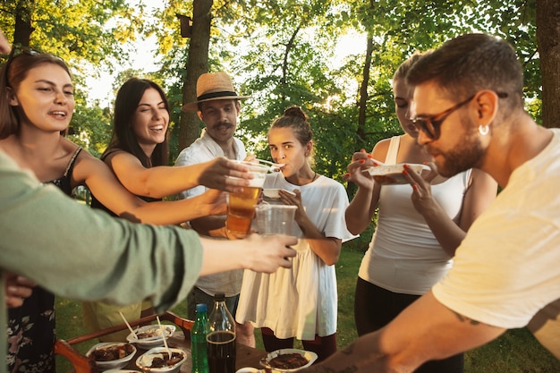 Foto grátis amigos felizes comendo e bebendo cerveja em um jantar de churrasco na hora do pôr do sol