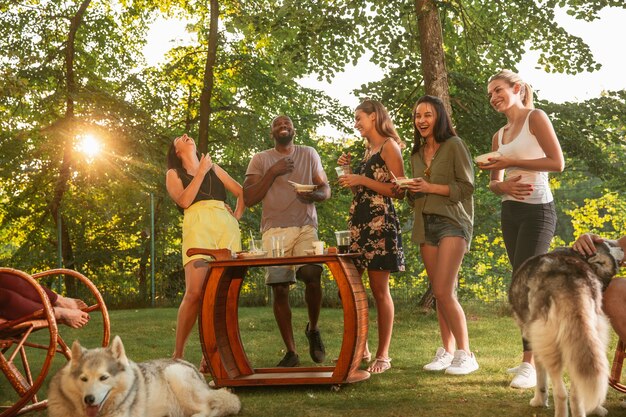 Amigos felizes comendo e bebendo cerveja em um jantar de churrasco na hora do pôr do sol