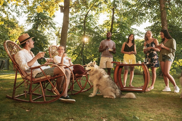 Amigos felizes comendo e bebendo cerveja em um jantar de churrasco na hora do pôr do sol