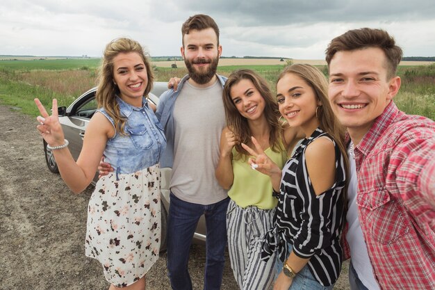 Amigos felizes em pé perto do carro tomando selfie