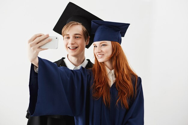 Amigos graduados da faculdade em caps sorrindo fazendo selfie.