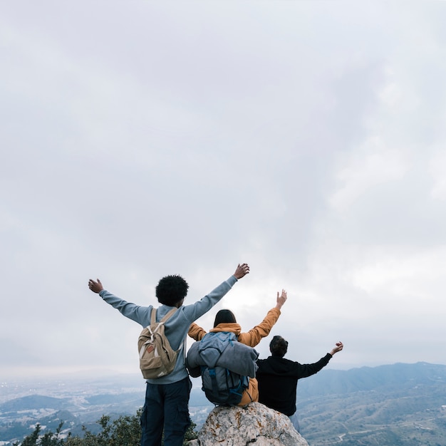 Amigos no topo da montanha, levantando os braços contra o céu nublado branco