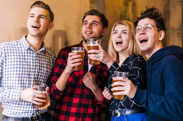 Amigos novos entusiasmado que apreciam a cerveja ao prestar atenção a algo