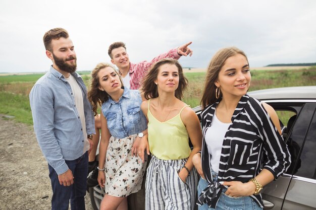 Amigos olhando homem apontando em algum lugar em pé perto do campo