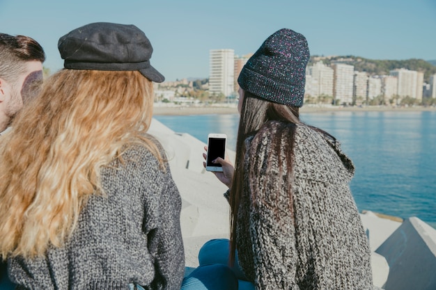 Amigos sentados ao lado do mar com smartphone