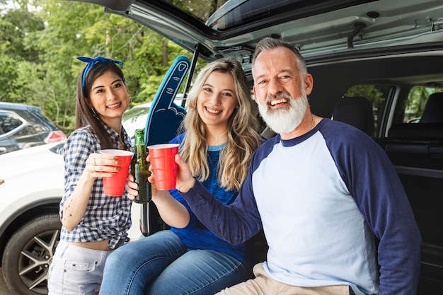 Amigos sentados e bebendo no porta-malas do carro em uma festa ao ar livre