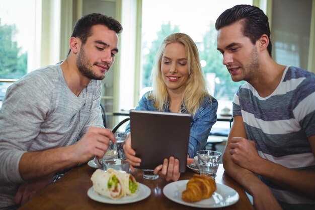 Amigos sentados na mesa e que usa a tabuleta digital no cafÃ ©