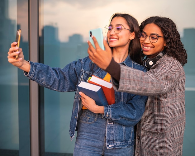 Amigos sorridentes com livros tirando selfies juntos