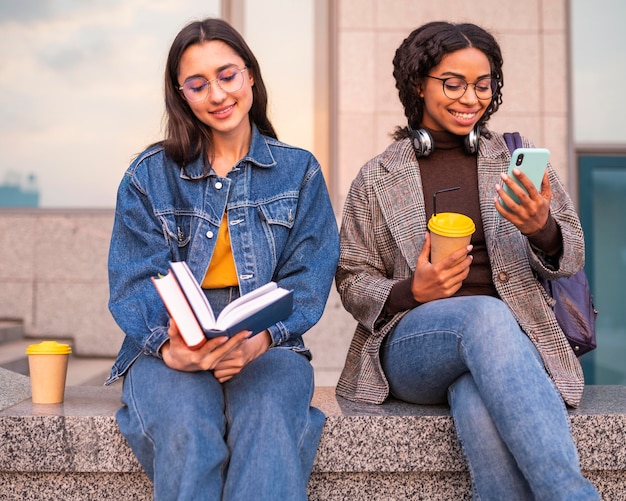 Amigos sorridentes com livros tomando café juntos do lado de fora