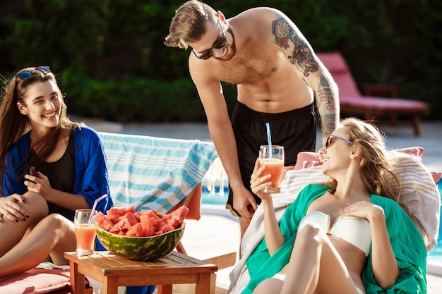 Amigos sorrindo, comendo melancia, bebendo cocktails, relaxando perto da piscina