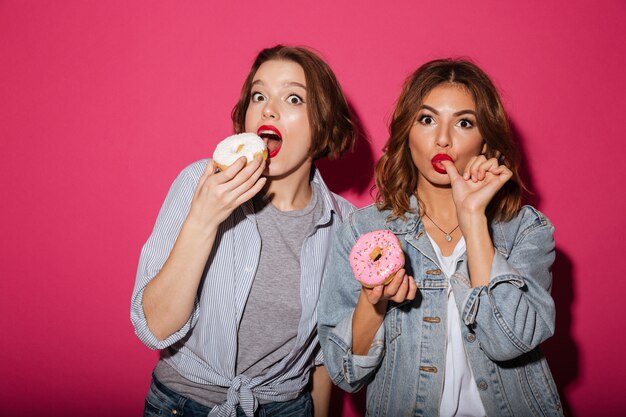Amigos surpreendentes de duas mulheres comendo rosquinhas
