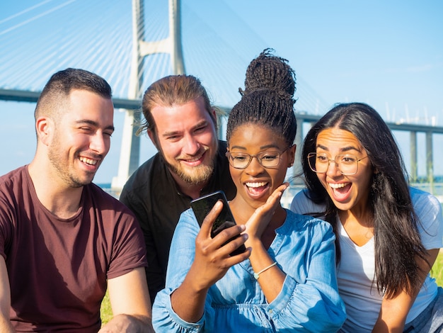 Foto grátis amigos surpresos usando smartphone ao ar livre