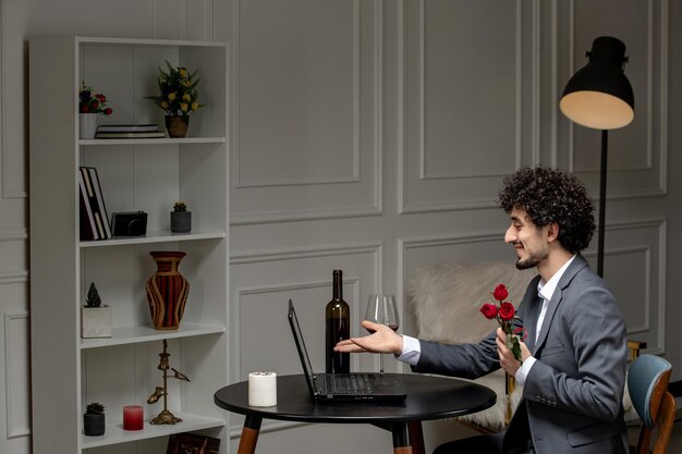 Amor virtual bonitão bonito de terno com vinho em um encontro de computador à distância segurando flores vermelhas