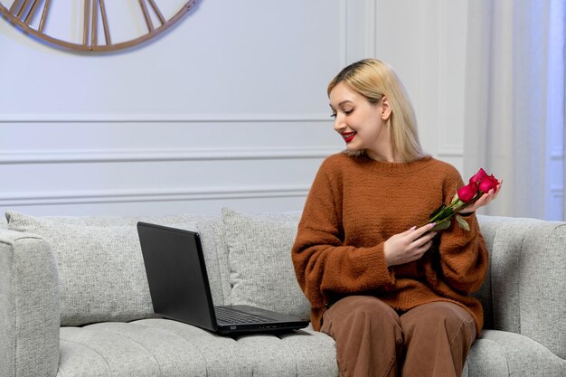 Amor virtual linda jovem loira em suéter aconchegante na data do computador à distância segurando flores vermelhas