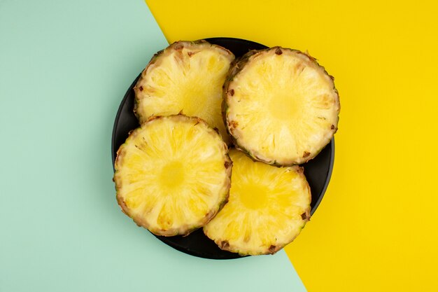 Anéis de abacaxi maduro suculento fresco dentro de chapa preta uma vista superior em uma mesa colorida