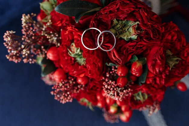 Anéis de casamento de ouro branco clássico no buquê vermelho