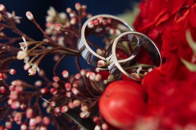 Anéis de casamento de ouro branco clássico no buquê vermelho