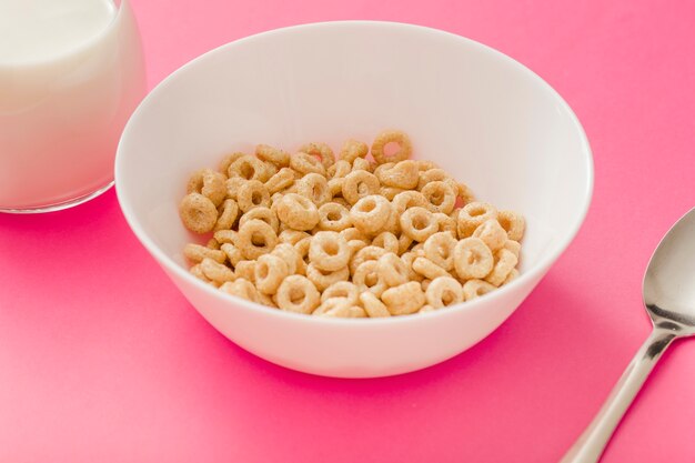 Anéis de cereais saudáveis ​​na tigela branca em fundo rosa