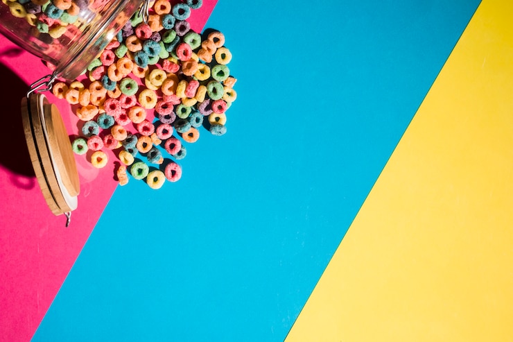 Foto grátis anéis de laço de cereais coloridos derramando de jar no pano de fundo colorido