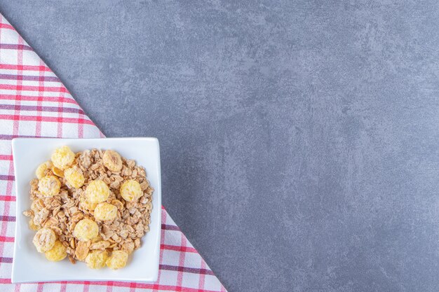 Anel de mel milho com muesli em uma tigela sobre um pano de prato, na mesa de mármore.