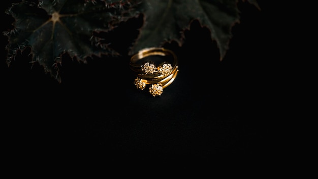 Anel de ouro feminino com flores e folhas e um fundo preto