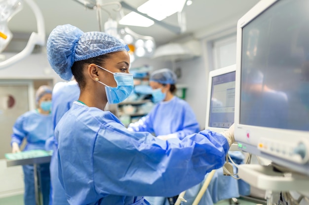 Anestesiologista verificando monitores enquanto seda o paciente antes do procedimento cirúrgico na sala de cirurgia do hospital paciente afro-americana adulta jovem está dormindo na mesa de operação durante a cirurgia