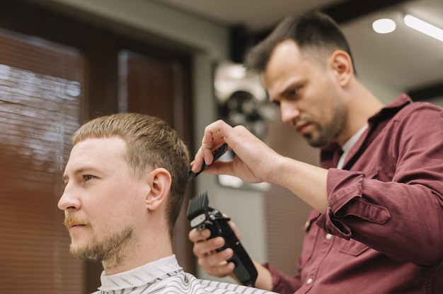 Ângulo baixo do cabeleireiro dando um corte de cabelo