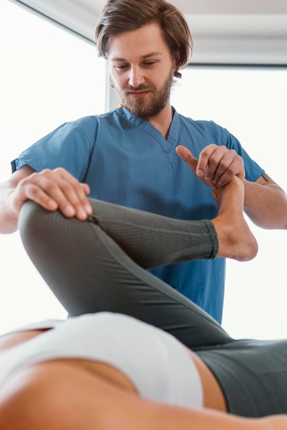 Foto grátis Ângulo baixo do terapeuta osteopático verificando o movimento da perna da paciente