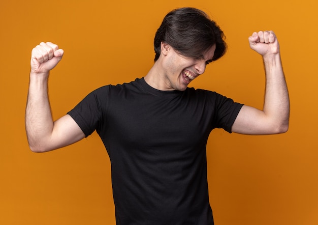 Animado com a cabeça baixa, jovem bonito vestindo uma camiseta preta mostrando um gesto de sim isolado em uma parede laranja