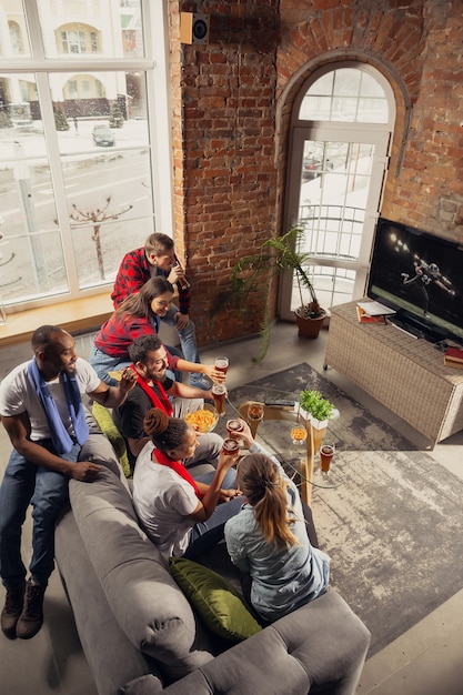 Animado grupo de pessoas assistindo futebol americano, jogo de esporte em casa.