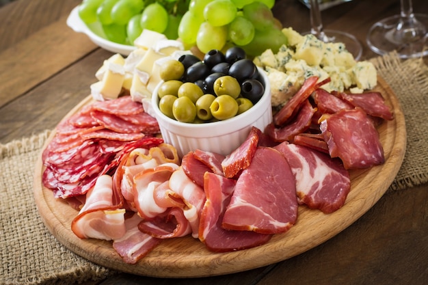 Foto grátis antepasto de catering prato com bacon, carne seca, salame, queijo e uvas em uma mesa de madeira