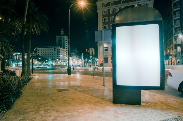 Anúncio em branco na calçada com semáforos turva à noite