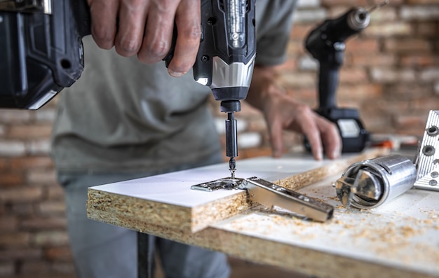 Aparafusar um parafuso autorroscante em um orifício de fixação de metal em uma tira de madeira usando uma chave de fenda, trabalho de um carpinteiro.