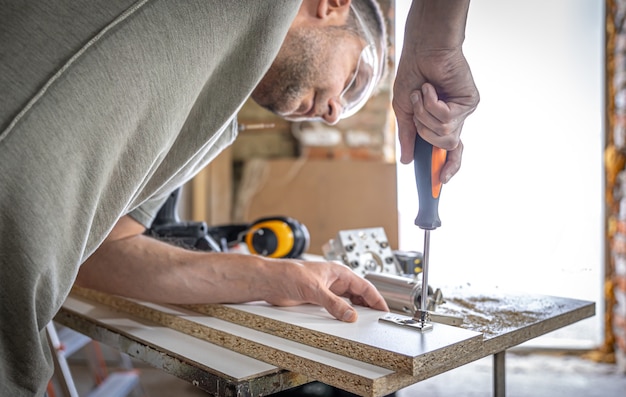 Foto grátis aparafusar um parafuso autorroscante em um orifício de fixação de metal em uma tira de madeira usando uma chave de fenda, trabalho de um carpinteiro.