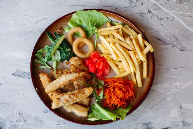 Aperitivos de restaurante saborosos para grandes empresas, incluindo nuggets de frango dourado, batatas fritas, folhas de salada verde e pepinos frescos, em pé na mesa branca, com uma aparência deliciosa de dar água na boca