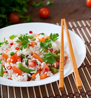 Apetitoso arroz saudável com legumes em chapa branca sobre uma mesa de madeira.