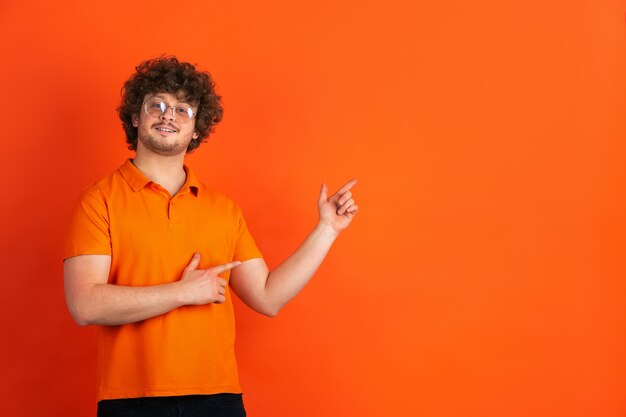 Apontando, escolhendo. Retrato monocromático de jovem caucasiano na parede laranja. Lindo modelo masculino encaracolado em estilo casual. Conceito de emoções humanas, expressão facial, vendas, anúncio.