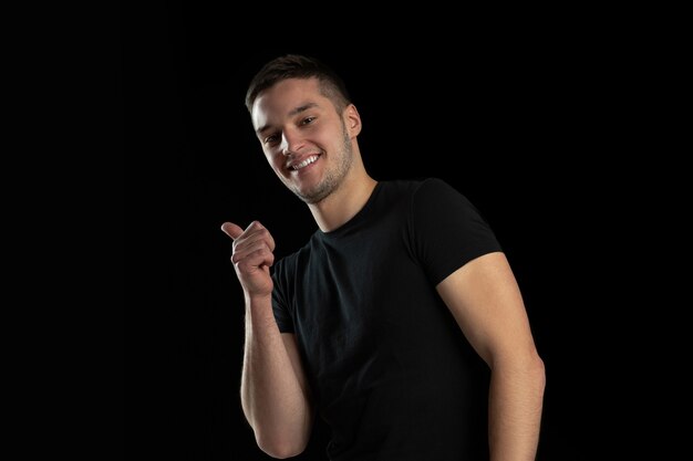 Apontando, sorrindo. Retrato monocromático de jovem homem caucasiano isolado na parede preta do estúdio.