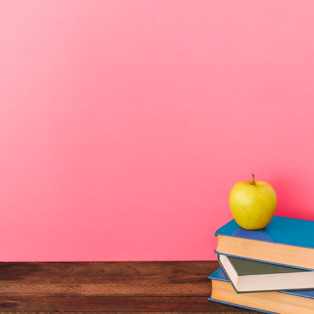 Apple e livros perto de parede rosa