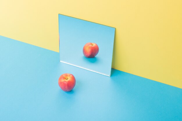 Apple na mesa azul isolada em amarelo perto de espelho