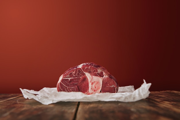 Apresentação de bife de perna angus cru em papel ofício branco mesa de madeira fundo vermelho